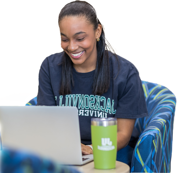 A smiling young woman sitting, using a laptop.